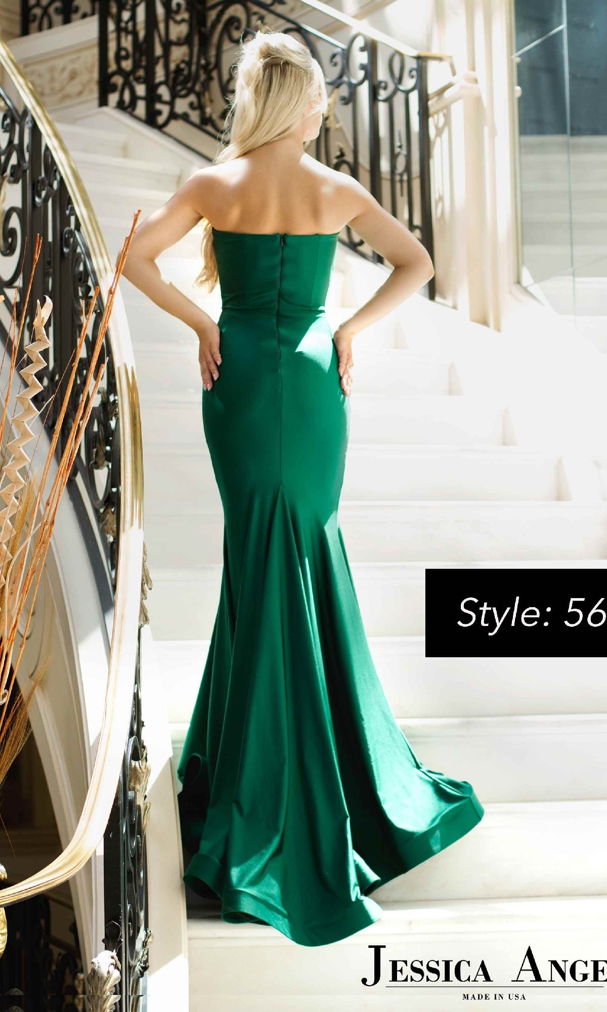 A woman faces away on a white staircase with ornate black railings, wearing the Strapless Long Mermaid Prom Dress: Jessica Angel 568 in emerald green.